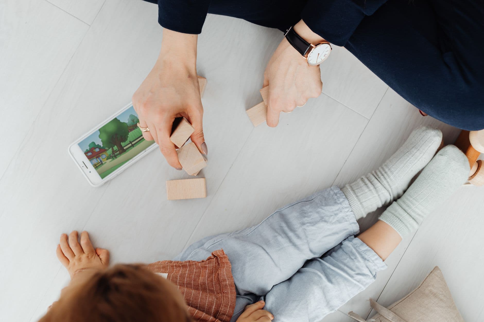 A young child and parent playing together with wooden blocks on the floor