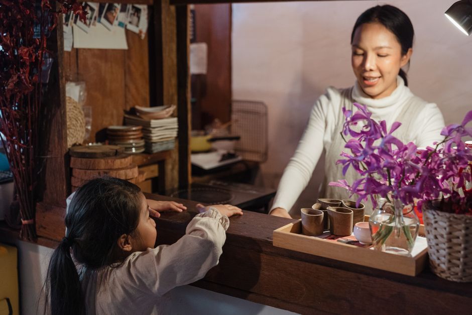 A mother in a kitchen talks with her young daughter across the bench