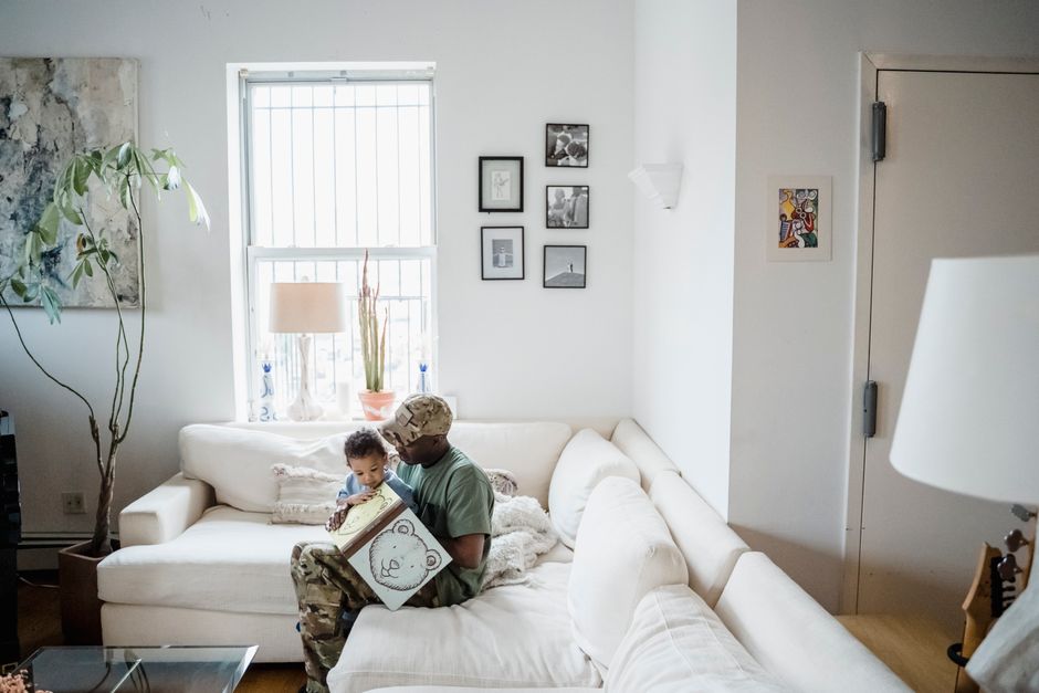 A father sits on a sofa and reads a picture book with his toddler